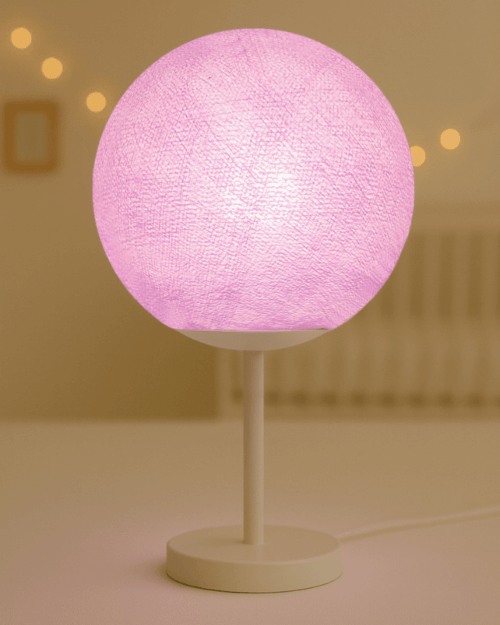 Violette Baumwollkugel-Tischleuchte mit LED auf weißem Fuß; weiches Lila-Licht setzt einen freundlichen Farbakzent auf Nachttisch oder Regal im Kinderzimmer.